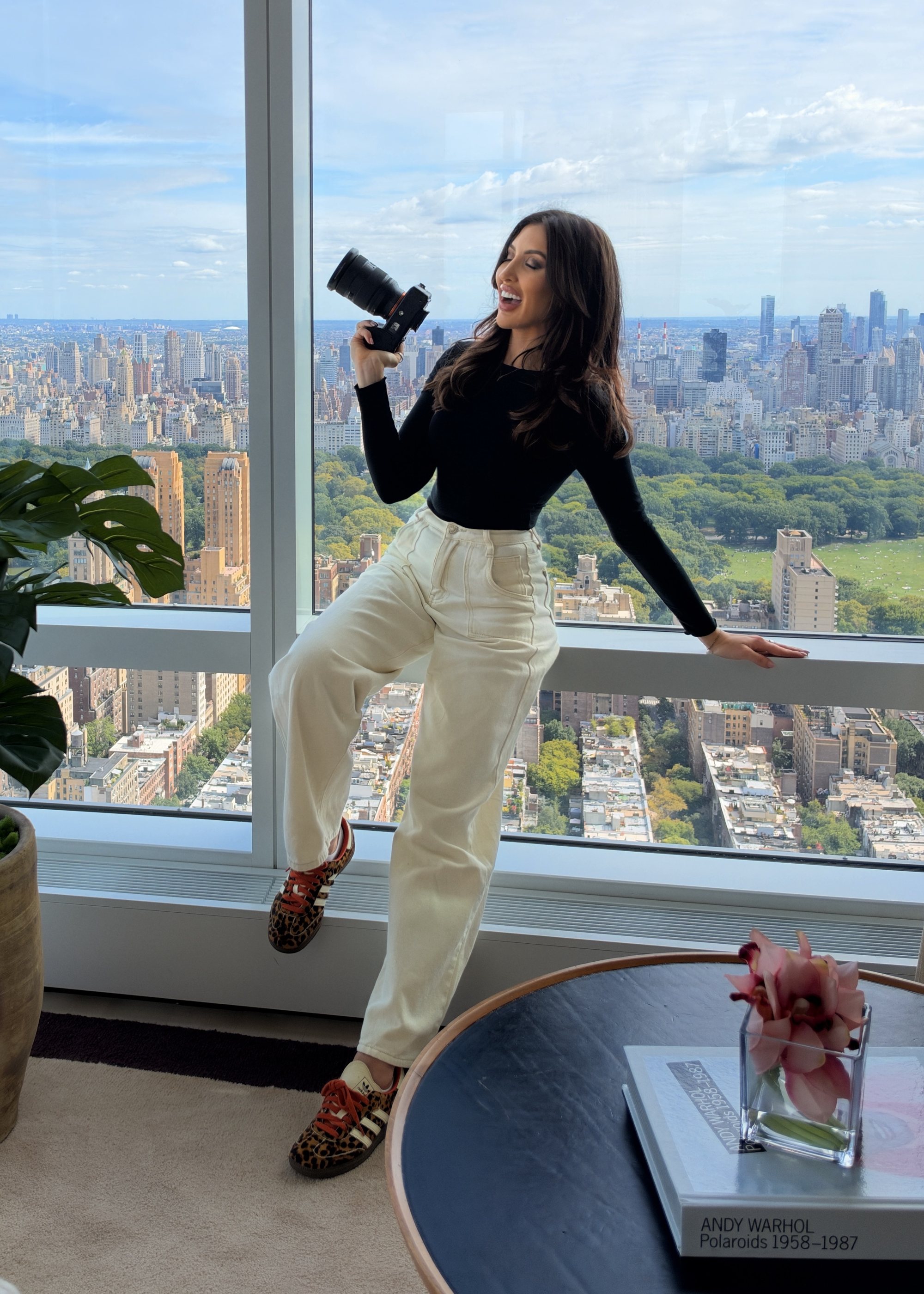 Sarah Cotty mid-laugh, camera raised, one foot on the ledge in leopard sneakers.