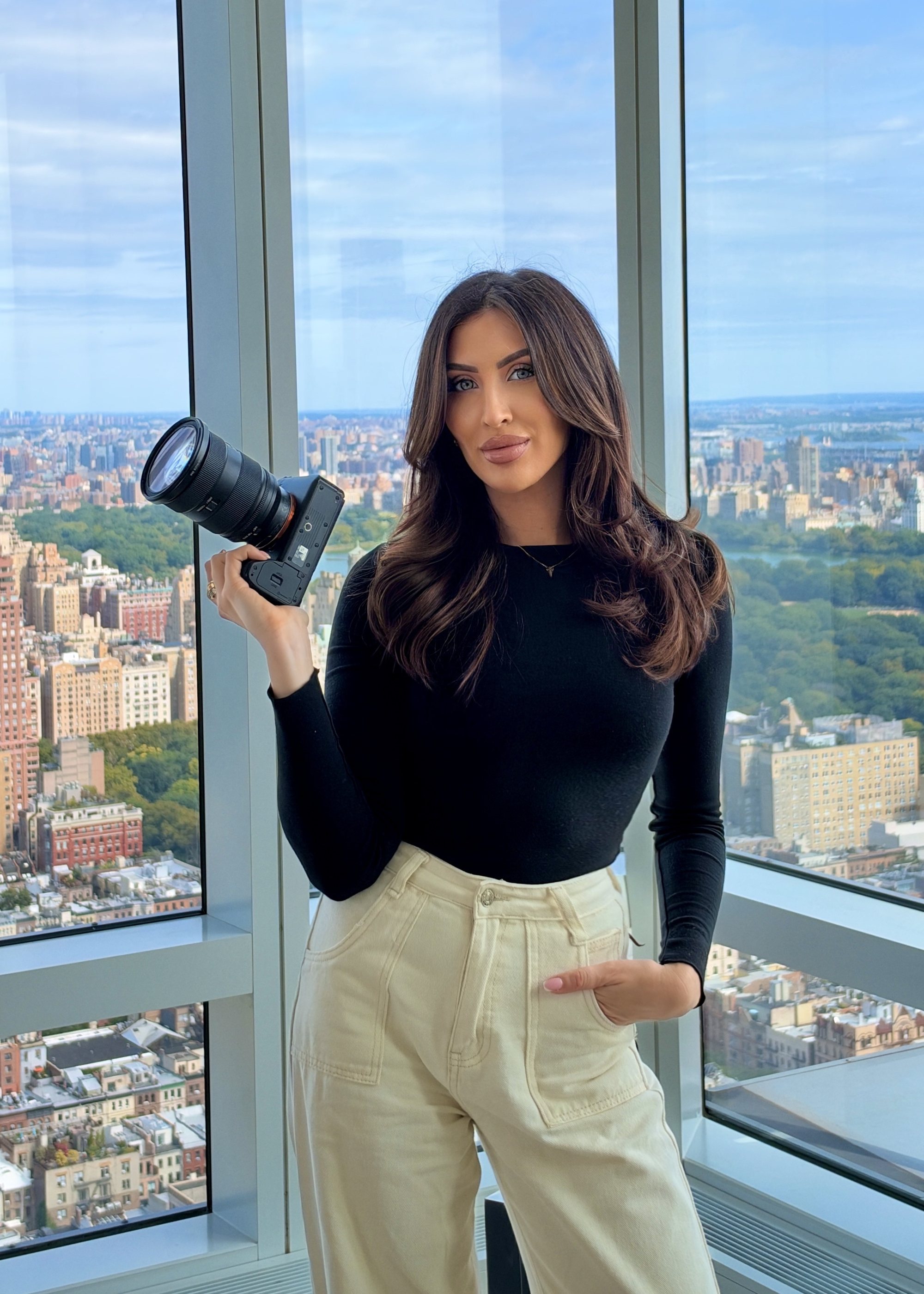 Sarah Cotty at a high window over Central Park, holding a camera.