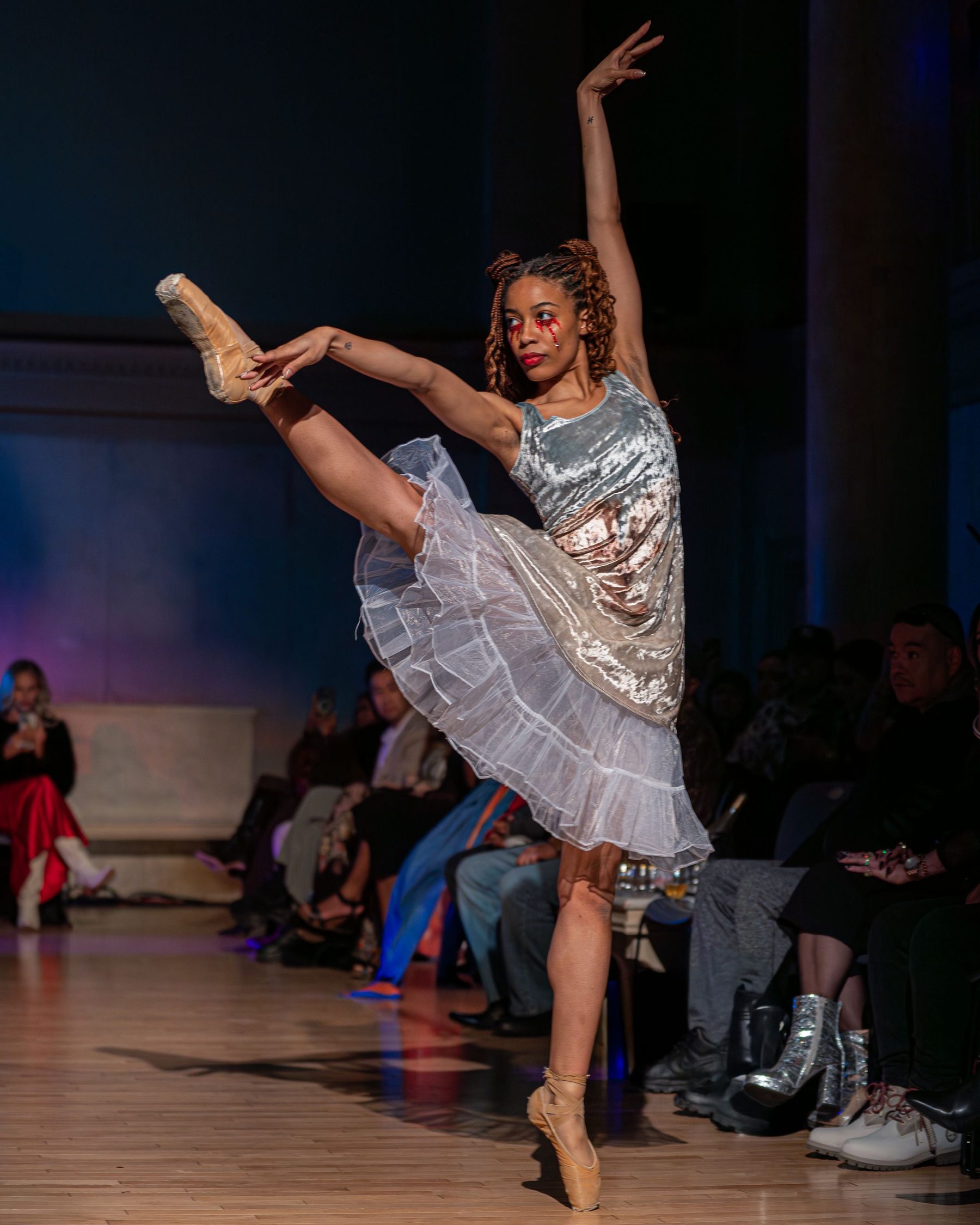 A dancer in a pale costume lifted on one leg on a stage.