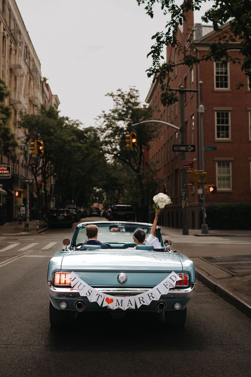 A bride and groom in a pale blue convertible, a Just Married banner across the trunk.